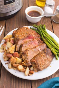 roast beef with potatoes and asparagus on a plate next to an instant pressure cooker