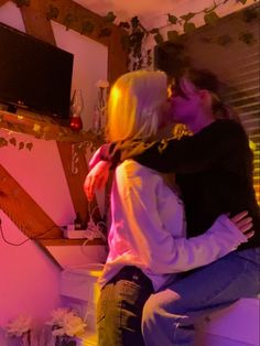 a man and woman kissing in front of a tv set with pink lights on the wall