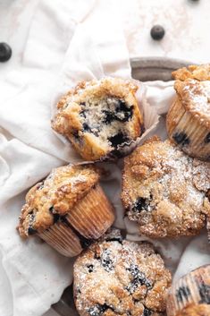 some blueberry muffins are sitting on a white cloth and there is powdered sugar on top