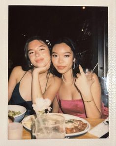 two young women sitting at a table with food and drinks in front of their faces