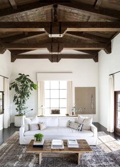 a living room with white couches and wooden beams on the ceiling, along with a large rug