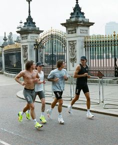 three men running down the street in front of an iron fence and gated area