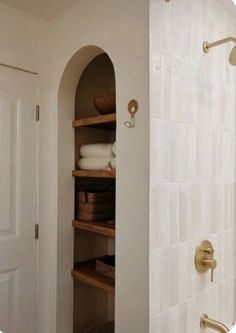 a bathroom with white tile walls and shelves filled with toilet paper, towels and baskets