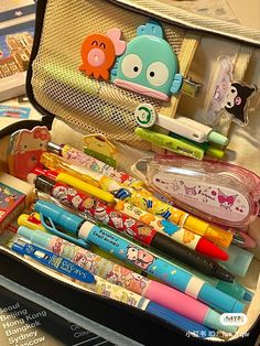 an open suitcase with pens, markers and other items in it sitting on a table