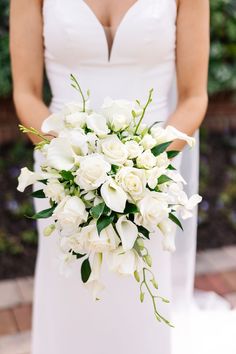 bridal bouquet with slight cascade. flowers are all white, and consist of roses, spray roses, calla lilies, and dendrobium orchids. Subtle accents of Italian ruscus add depth as an accent of greenery Lilly Bouquet Wedding, White Calla Lily Wedding Bouquet, Calla Lillies Wedding, All White Bridal Bouquet, Calla Lily Wedding Flowers, White Wedding Flowers Bouquet, White Calla Lily Bouquet, White Orchid Bouquet