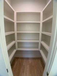 an empty walk in closet with white shelving and wood flooring is seen from the inside