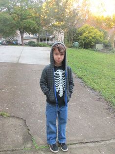 a young boy wearing a skeleton hoodie standing in front of some grass and trees