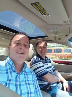 two men sitting in the back seat of a car, one smiling at the camera