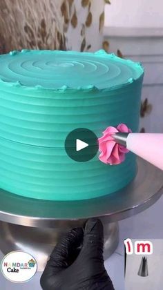 a person in black gloves is decorating a cake with blue frosting and pink flowers