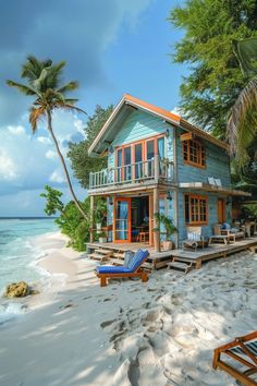 a blue house sitting on top of a sandy beach next to the ocean and palm trees