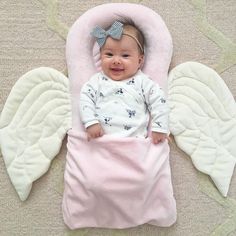 a baby laying on top of a pink blanket next to an angel wings shaped pillow