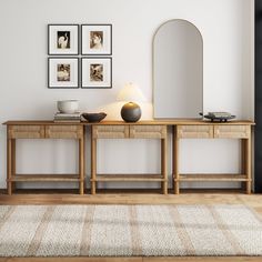 a wooden table sitting next to a white wall with pictures on it and a lamp