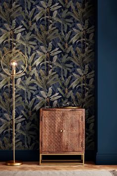 a wooden cabinet sitting in front of a wall with leaves on it and a floor lamp next to it