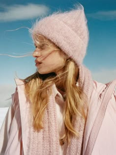 a woman with blonde hair wearing a pink hat and scarf over her shoulders, looking off into the distance