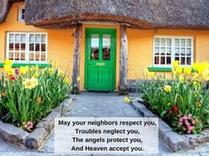 a green door and some flowers in front of a yellow house with thatched roof