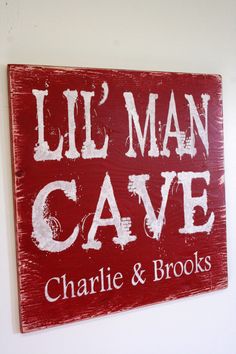 a wooden sign that says lil man cave on the side of a white wall with red and white lettering