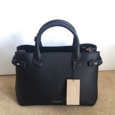 This Is The Burberry Banner Tote Bag In Black, Made With A Combination Of Leather And Canvas Check Materials. It Features The New Model Wide Shoulder Strap In Black, Gold Hardware Accents, And A Spacious Interior With Inner Pockets. The Bag Has A Classic Checkered Pattern And A Sleek Design That Would Complement Any Outfit. It Is A Great Addition To Any Collection And Would Make An Excellent Gift. It Is An Authentic High-Quality Bag That Is Both Stylish And Functional. Elegant Satchel With Branded Hardware, Elegant Office Bags With Branded Hardware, Black Luxury Tote Satchel For Everyday, Elegant Satchel Bag With Branded Hardware, Elegant Satchel With Branded Hardware In Tote Shape, Elegant Tote Satchel With Branded Hardware, Elegant Shopping Bags With Branded Hardware, Black Satchel With Branded Hardware For Everyday Luxury, Elegant Black Satchel With Branded Hardware