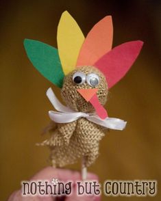 a hand holding a small toy turkey with a bow on it's head and wearing a white ribbon around its neck