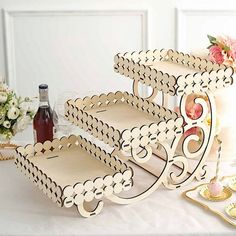 three tiered wooden trays on a table with flowers and wine bottles in the background