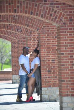 a man and woman standing next to each other in front of a brick wall with an archway