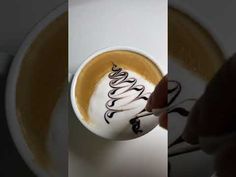 a person holding a spoon over a cup with liquid in it and writing on the foam