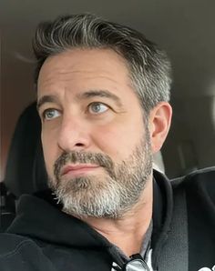 a man with grey hair and beard wearing a black hoodie