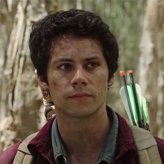 a young man holding two arrows in his right hand and looking at the camera with an angry look on his face