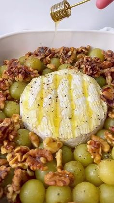 grapes and walnuts in a white bowl being drizzled with honey syrup