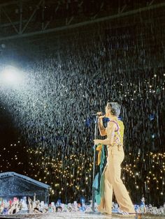 a man standing on top of a stage under a rain covered sky holding an umbrella