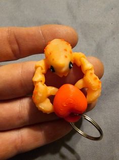 a hand holding a ring with an orange crab in it's mouth and a piece of fruit on the other side