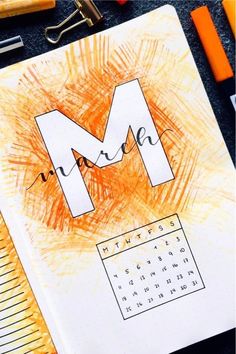 a notebook with the letter m drawn on it and some markers next to it,