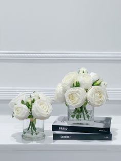 two vases filled with white roses sitting on top of a book next to each other