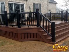 a wooden deck with black railing and handrails in front of a brick house