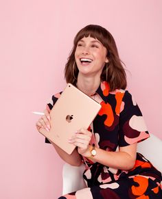 a woman sitting on a chair holding an apple laptop in her hands and smiling at the camera