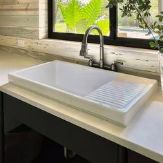 a white sink sitting under a window next to a vase filled with green plantes