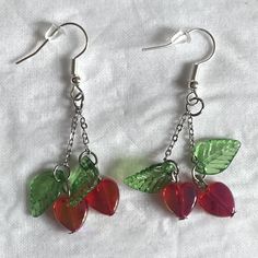 two cherries with green leaves hang from silver earwires on a white sheet