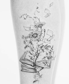 a black and white photo of a book with flowers coming out of it on the thigh