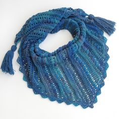 a blue crocheted scarf with tassels on it sitting on a white surface