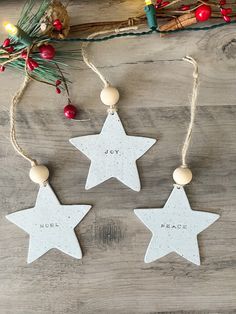 three white ceramic stars hanging from twine on wooden table next to christmas tree decorations