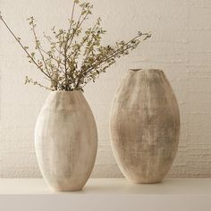 two white vases with plants in them on a shelf next to a brick wall