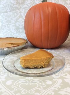 a piece of pumpkin pie sitting on top of a glass plate next to an orange pumpkin