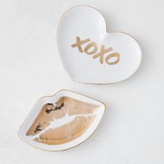 two heart shaped dishes with the word xoxo painted on them, one white and one gold