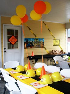 the table is set up with yellow and orange balloons in the shape of hard hats