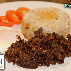 a plate with rice, meat and eggs on it next to some tomatoes in the background