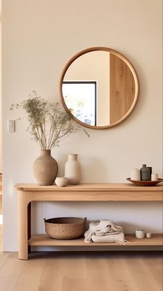 a wooden table with a mirror and vases on it next to a white wall