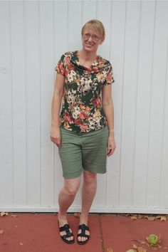 a woman standing in front of a white wall wearing green shorts and a floral shirt