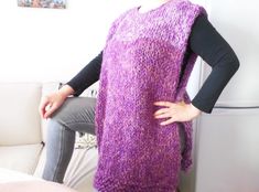 a woman standing next to a couch wearing a purple sweater