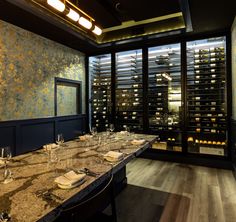 a long table with wine glasses and place settings in front of a window filled with bottles