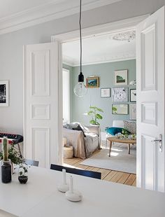 an open door leading to a living room and dining room with white walls, wood floors and furniture