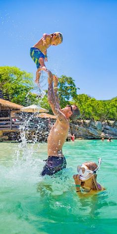 two people are playing in the water with a boy on his shoulders and another person standing up above them